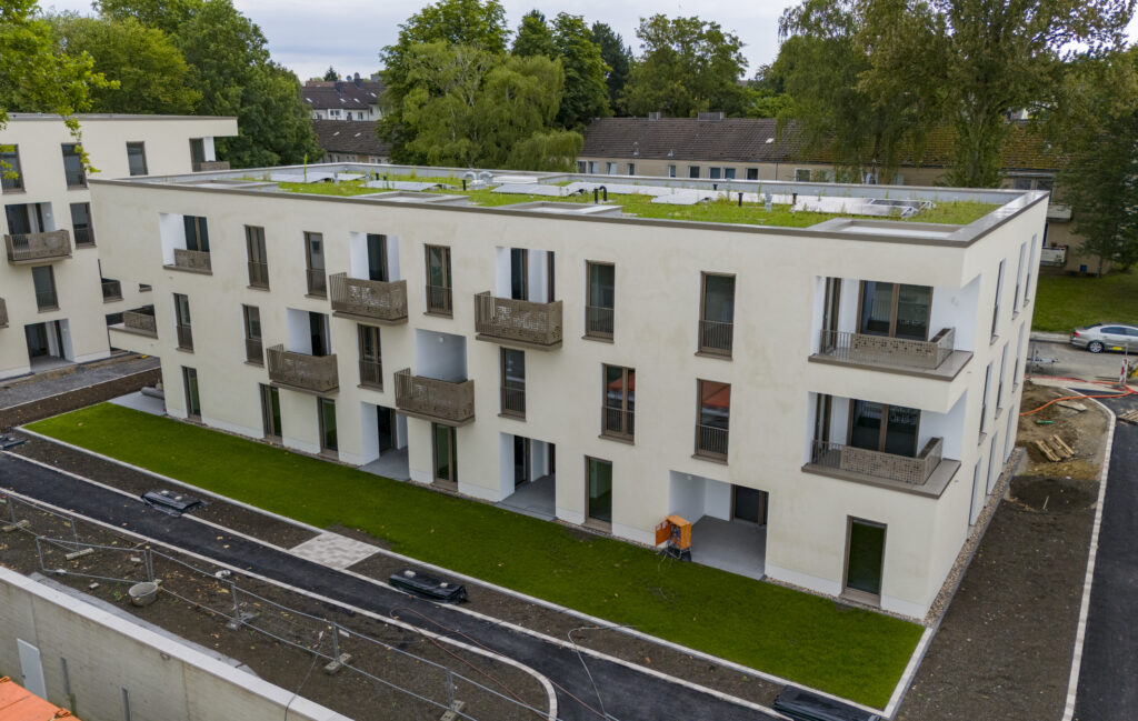 Schräge Luftaufnahme eines Neubaus mit heller Fassade, Balkonen, Gründach und Außenanlagen im Bau